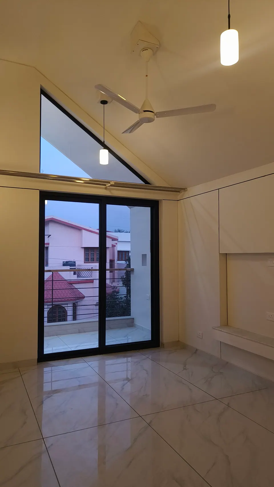 Room with a triangular gable window above a black-framed sliding door to a balcony