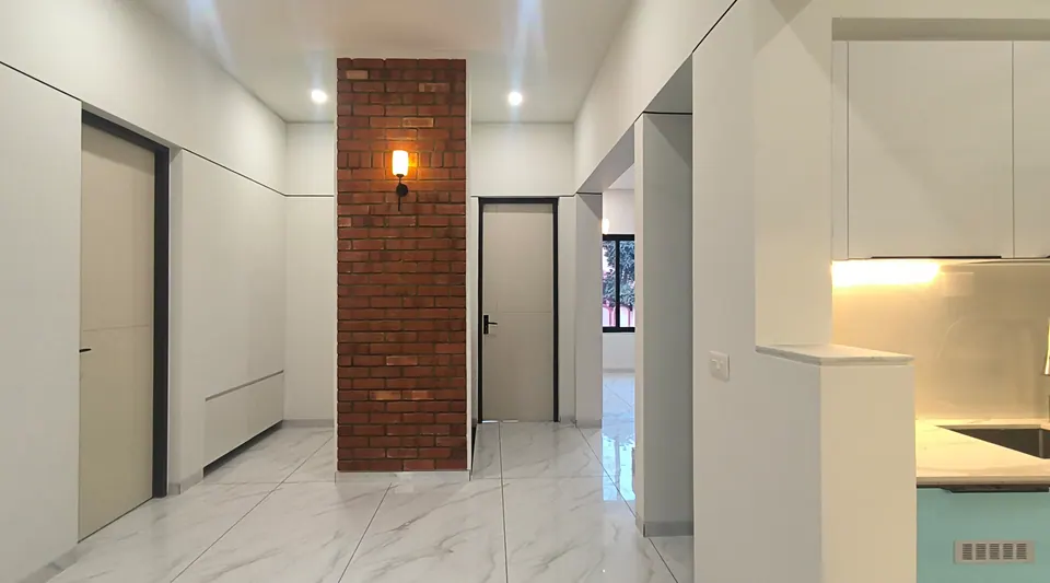 Hall with an exposed-brick column and wall lamp, white doors and a glimpse of a kitchen with mint-green cabinets