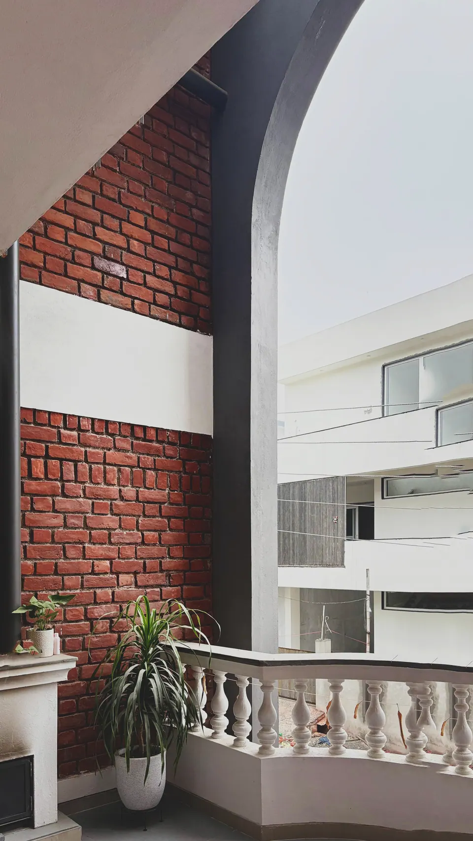 Brick wall and the grey arch beside a curved white balustrade, a potted plant on the balcony