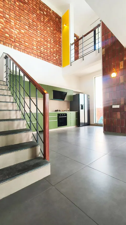 Double-height space with a stair, brick walls, a yellow slot and the green kitchen at the far end