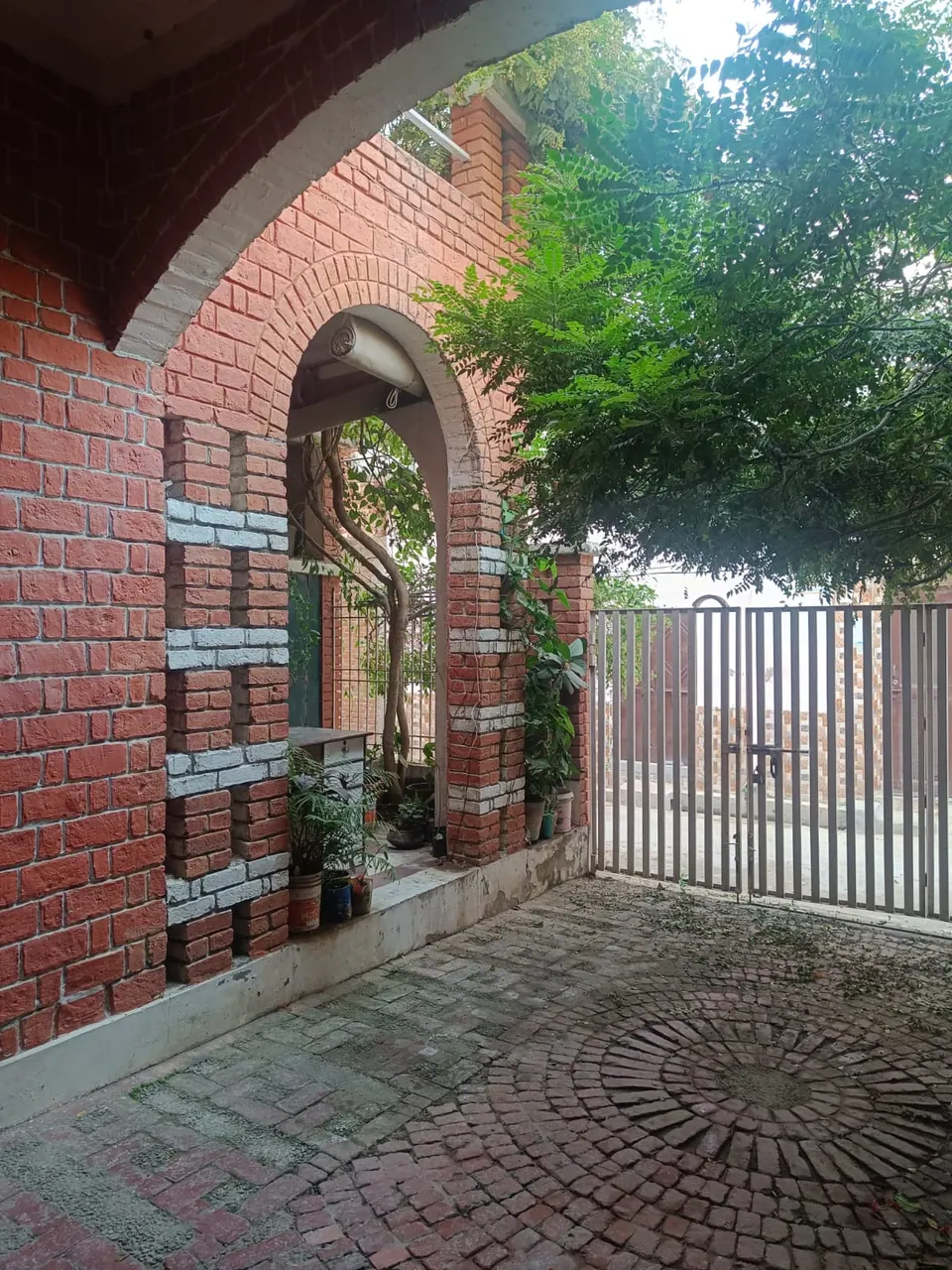 Brick arch framing a yard of circular brick paving, a pierced brick wall with white bands and the gate beyond