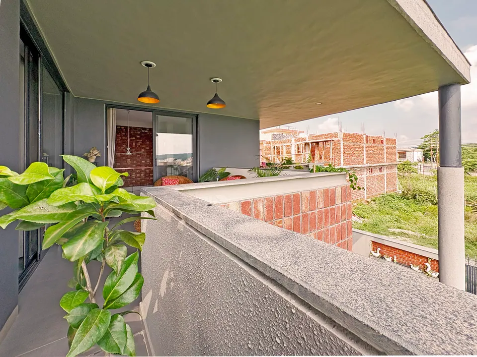 Upper covered terrace with pendant lamps, a grey parapet and a brick-clad wall, neighbouring houses beyond