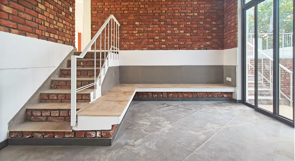 Stair with brick-faced steps and a white railing rising to a timber-topped landing beside full-height glazing