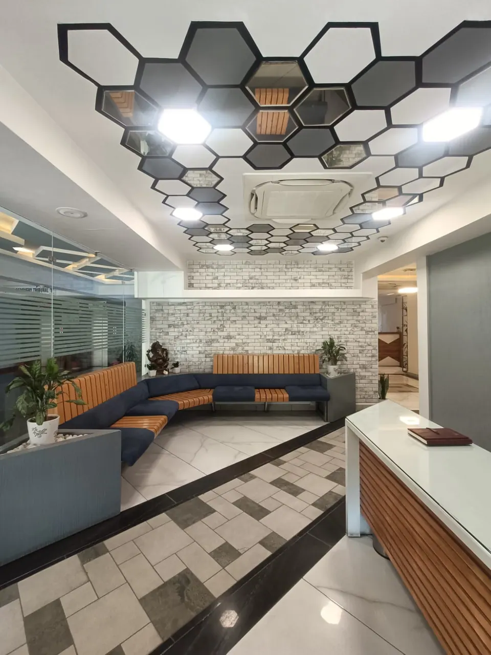 Reception with a hexagonal mirrored ceiling, a timber-slatted counter and the curved blue sofa along a brick-effect wall