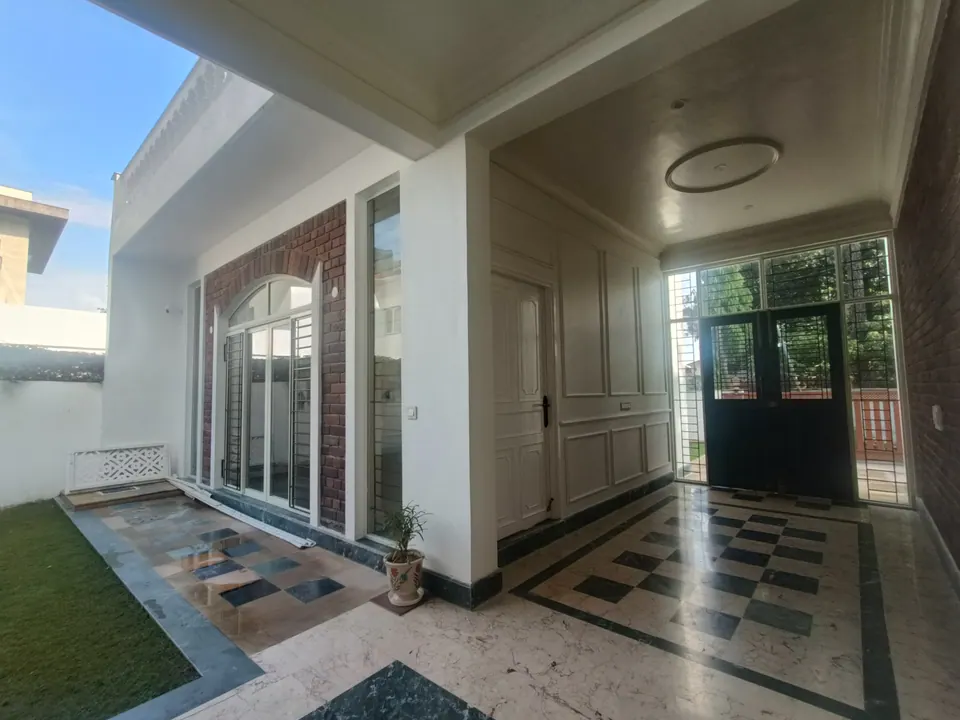 Verandah with a black and white chequered marble floor, glazed double doors and an arched window in exposed brick beside the lawn