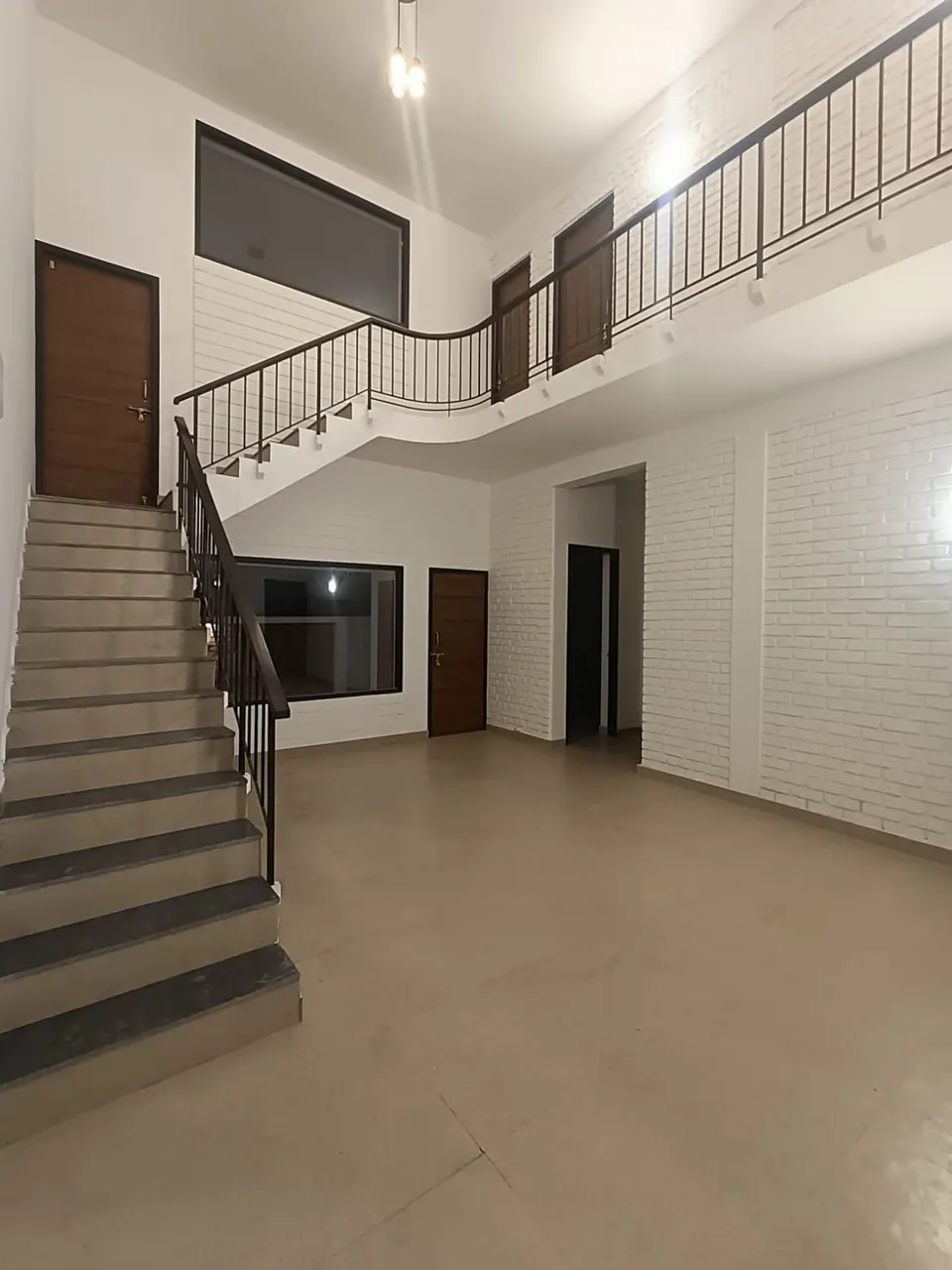 Stair with a black railing rising to a curved upper gallery beside white-painted brick walls