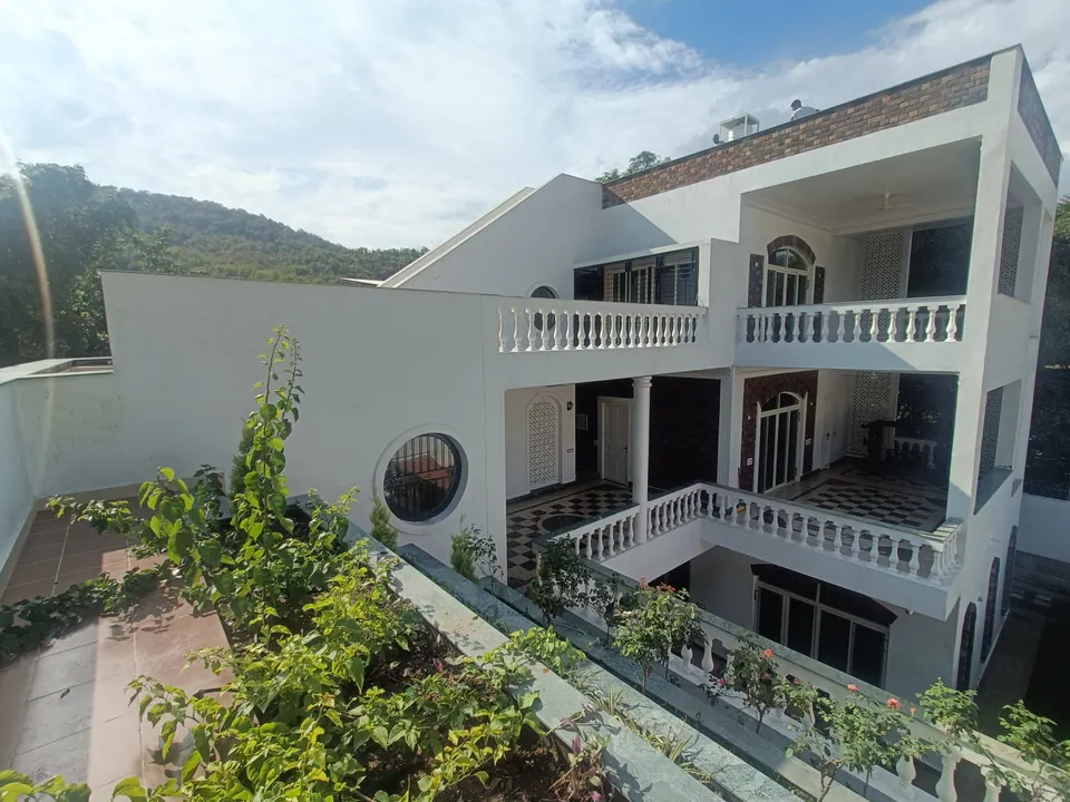 The house from the upper terrace: white balustraded galleries around the courtyard, a round window and wooded hills behind