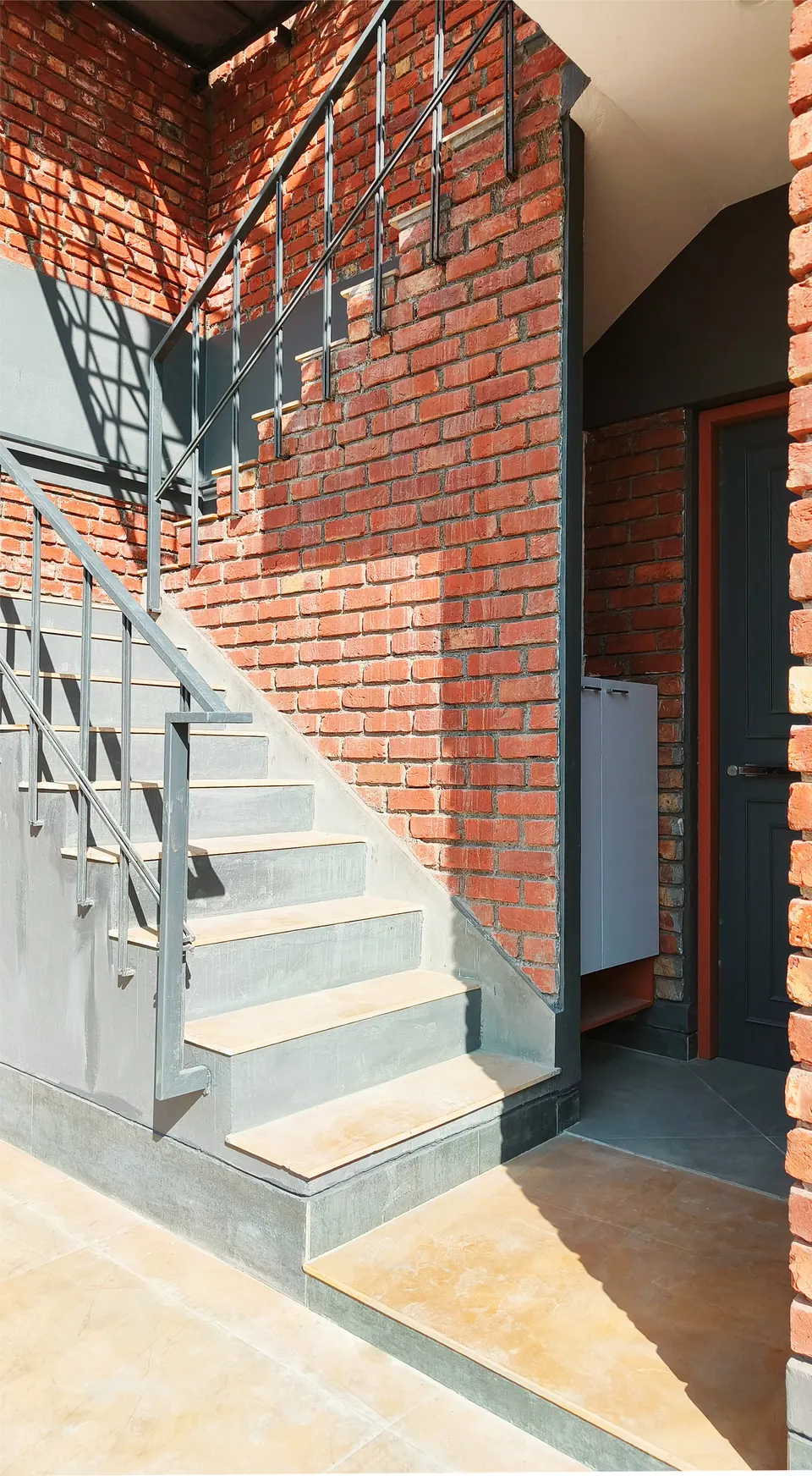 Stair with a steel railing rising along a brick wall beside a recessed entrance door