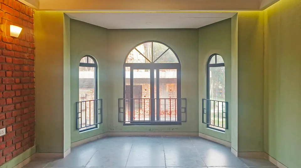 Room with sage-green walls and a bay of three arched windows with black steel balconettes, a brick wall at left