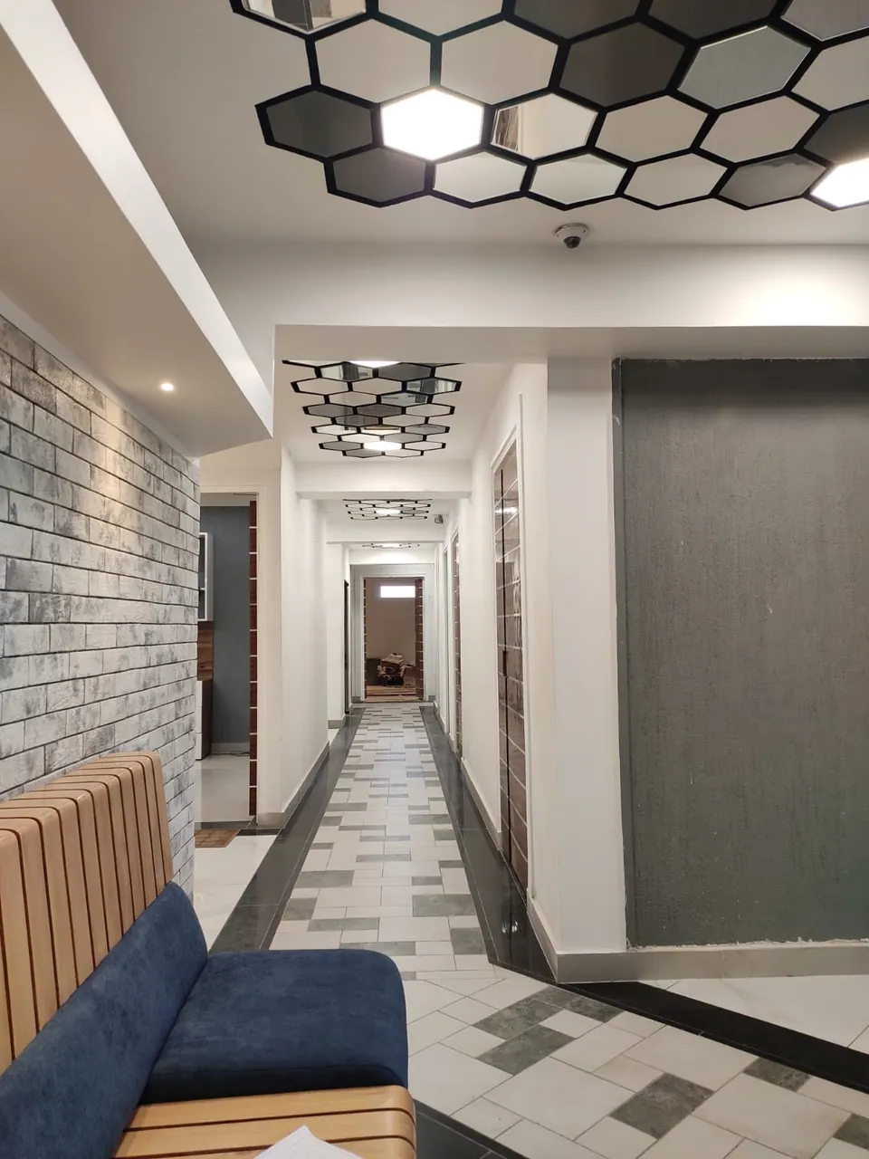 Corridor beside a brick-effect wall under hexagonal ceiling panels, the blue sofa in the foreground