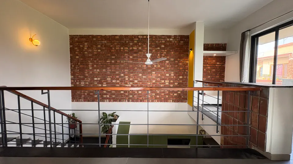 Gallery railing across the double-height space with a brick wall beyond, the green kitchen visible below