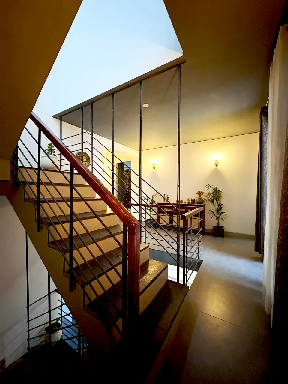 Stairwell with a timber handrail and black railings beneath an open skylight, lit by wall lamps