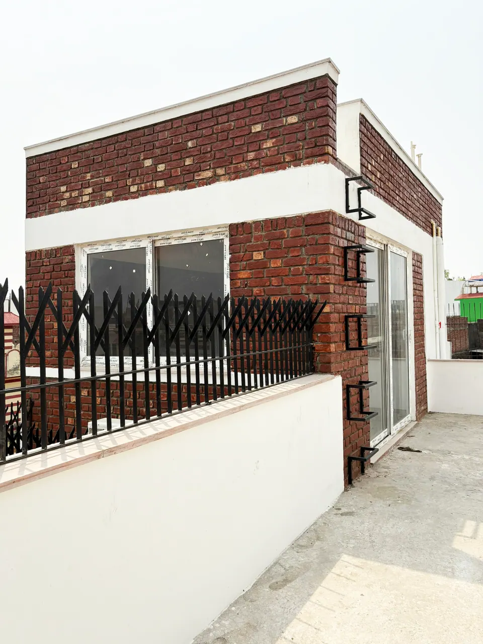 Roof terrace: a brick-clad room with a white parapet, a glazed door and a black decorative railing on a white wall