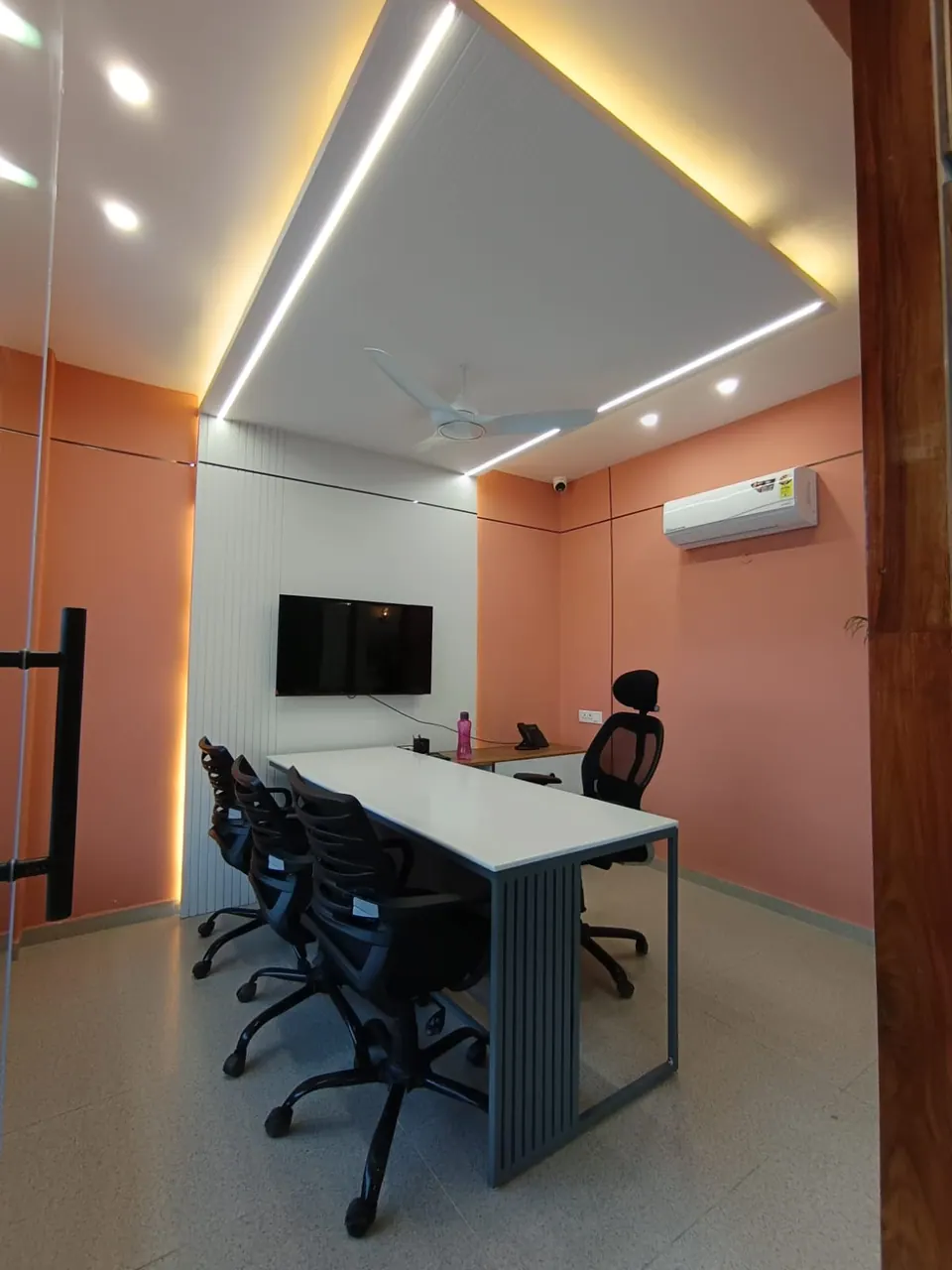 Cabin with coral walls, a white table with black mesh chairs, a wall-mounted TV and linear ceiling lights