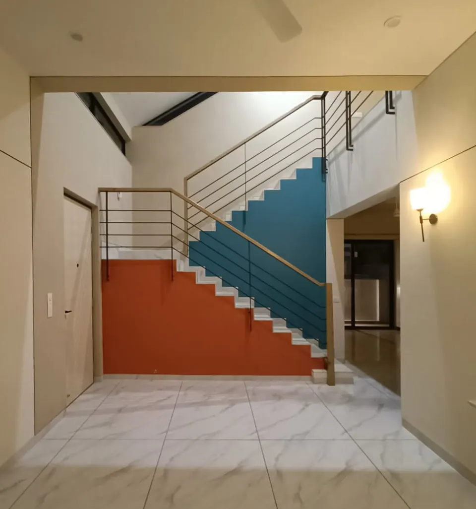 Stair hall: coral and teal painted walls under a stair with a timber handrail and black steel balusters, marble floor
