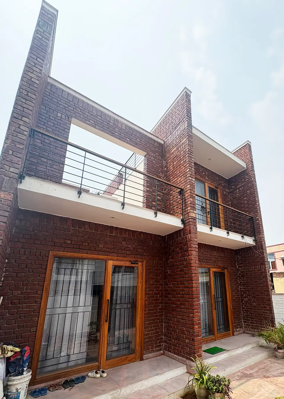 Angled view of the brick facade, its balconies and the framed opening at the upper level, seen from the forecourt