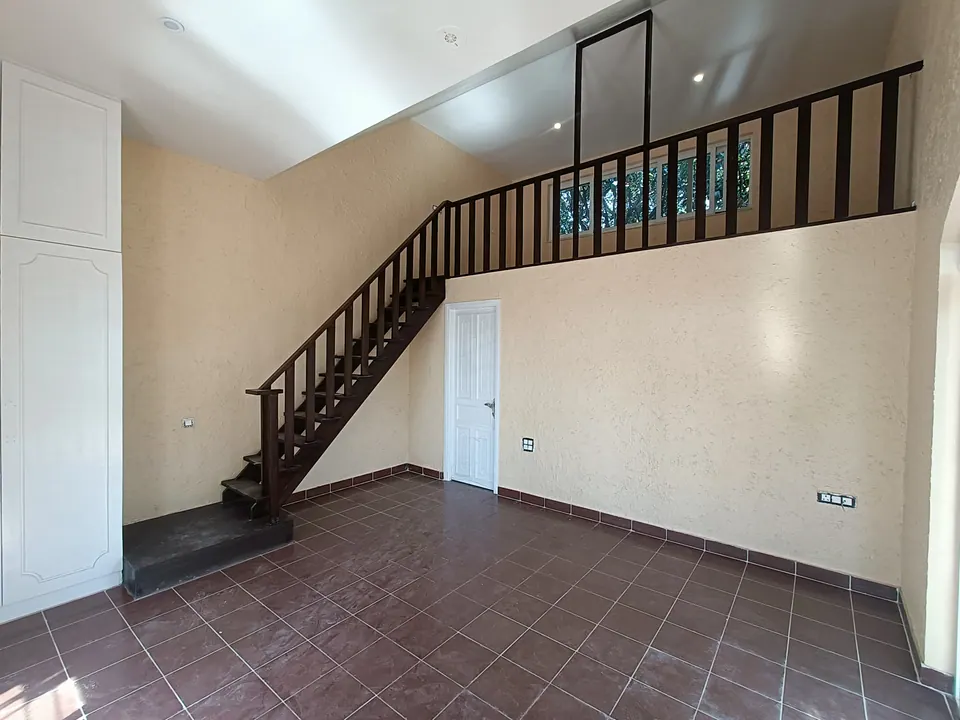 Room with a dark timber stair rising to a mezzanine gallery, textured cream walls and a terracotta tile floor