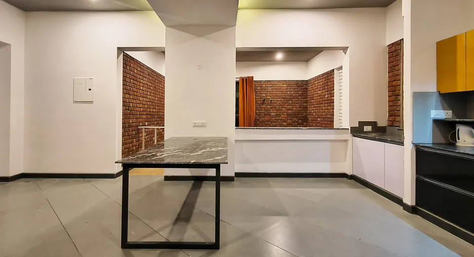 Dining area with a stone-topped table beside a column, brick-framed openings to the next room