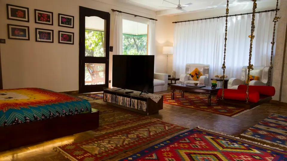 Bedroom and sitting area: bed, low media unit, white armchairs, a swing with red bolsters, white curtains and patterned rugs