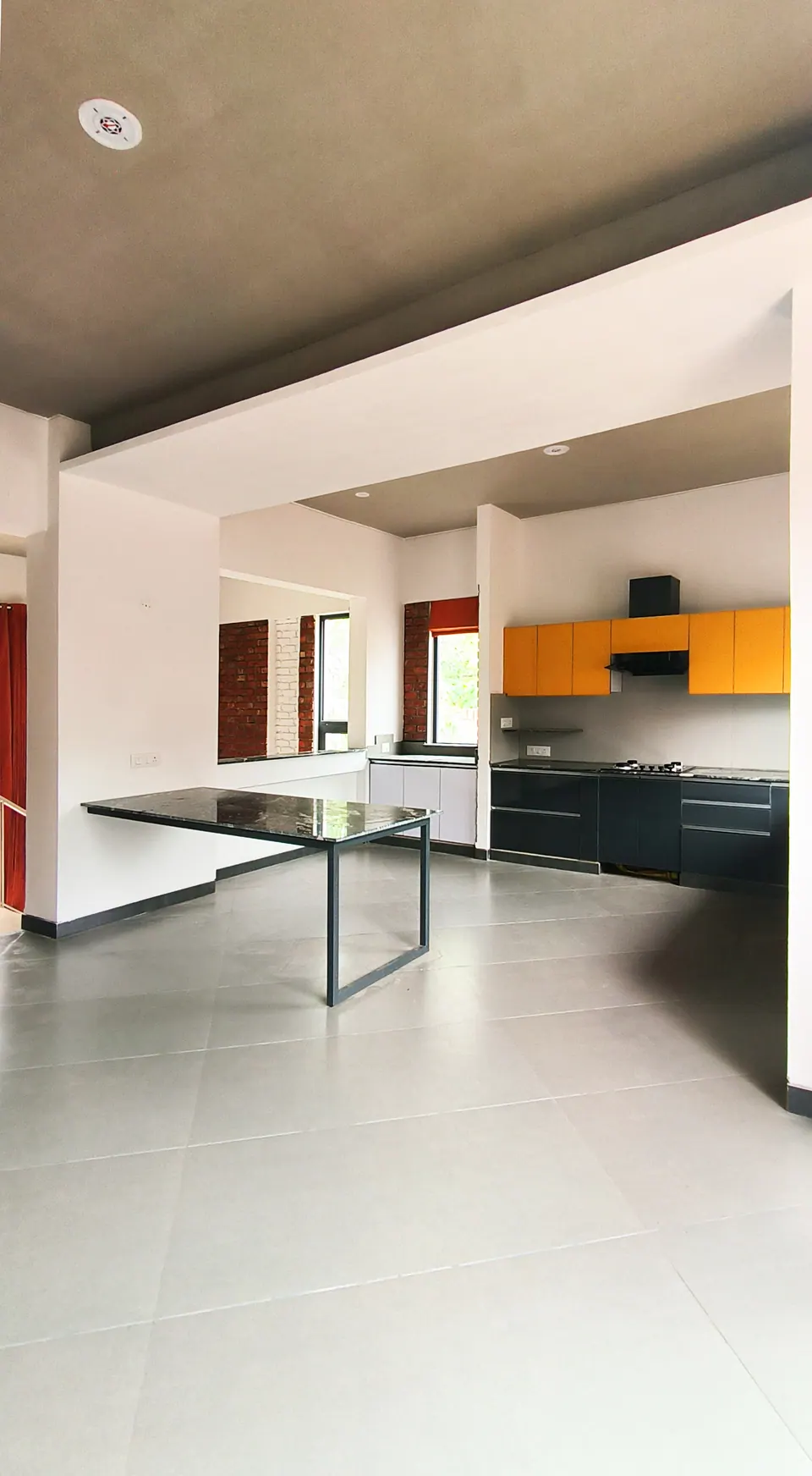 Open kitchen with yellow wall cabinets and black base units, a stone-topped dining table in front