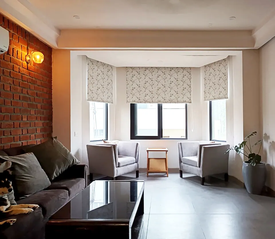 Sitting room with a brick wall and lamp, a dark sofa with a sleeping dog and two armchairs in a bay window