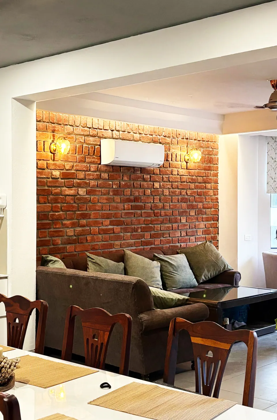 Sofa and dining chairs before an exposed-brick wall with wall lamps and an air conditioner