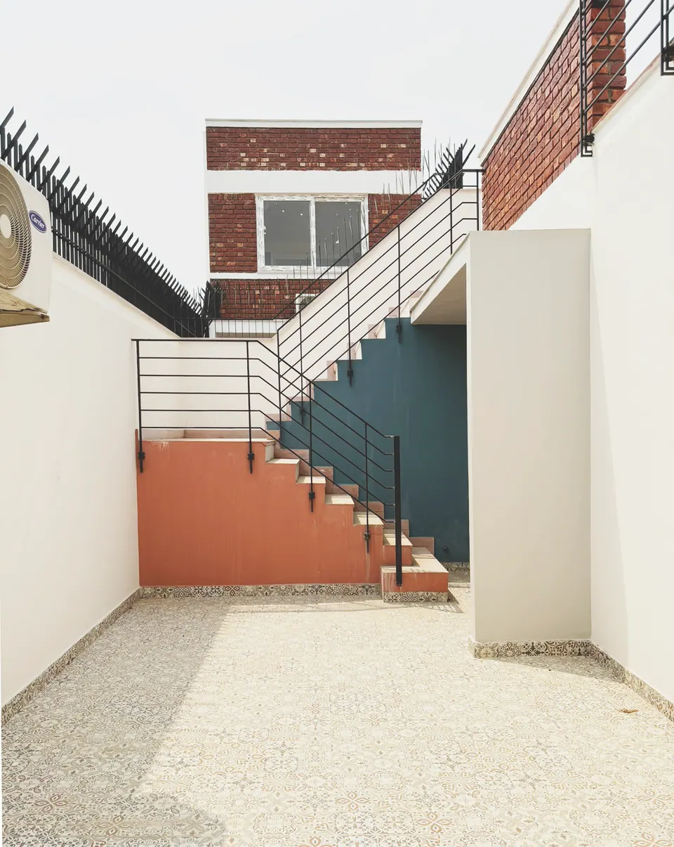 Side yard with an external stair and black railing along a white wall, salmon and teal painted walls beneath, brick volume above