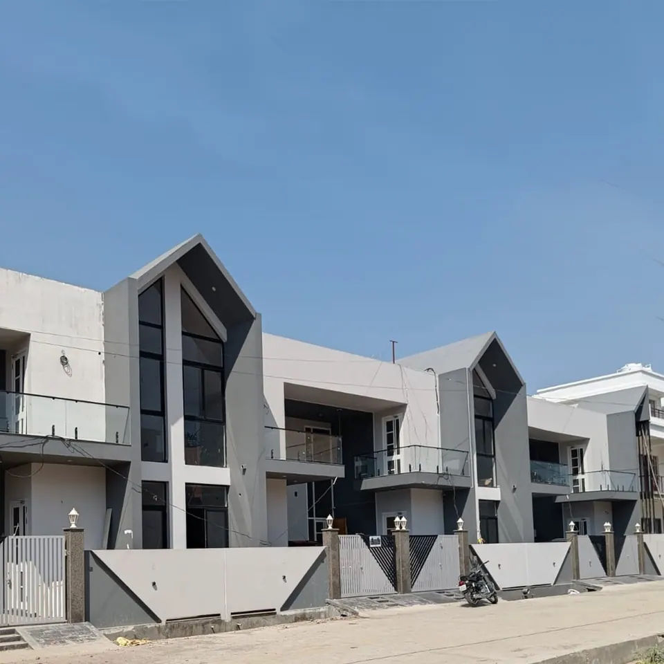 Row houses seen along the street: repeated grey gabled bays with tall glazing above patterned boundary walls and gates