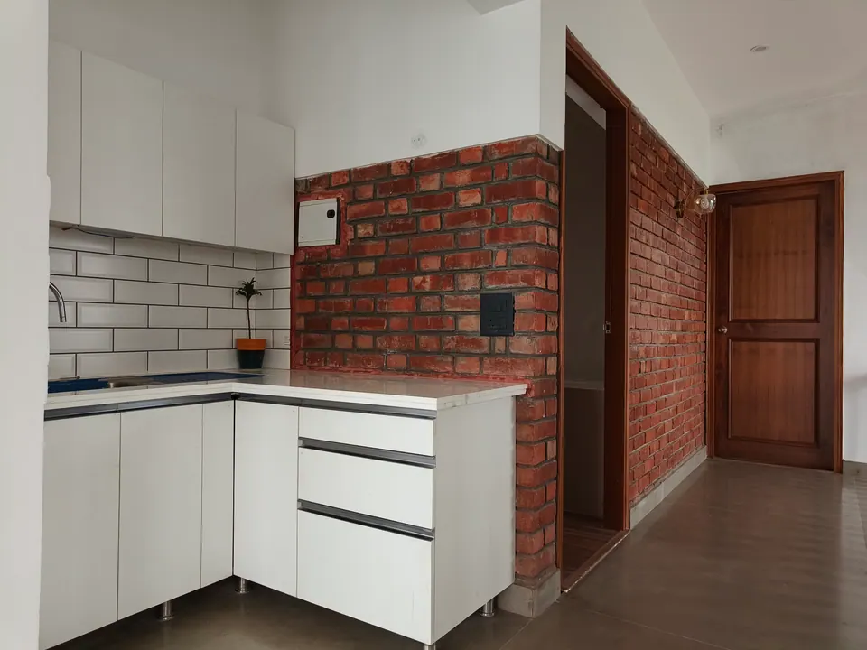 Kitchen with white cabinets and subway tiles beside an exposed brick wall and a timber door