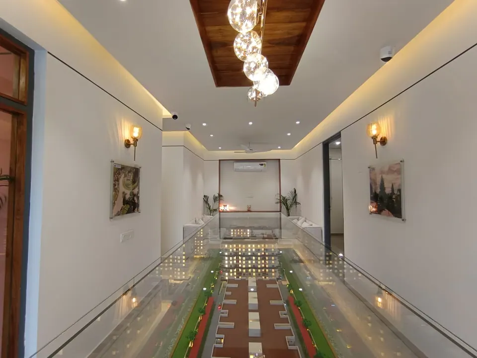 Gallery with a long glass-covered scale model of the housing, framed renders on the walls and a cluster of glass pendants