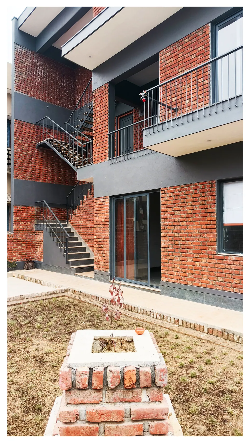 Brick house across a newly planted lawn, a brick plinth planter in the foreground and a glazed sliding door behind