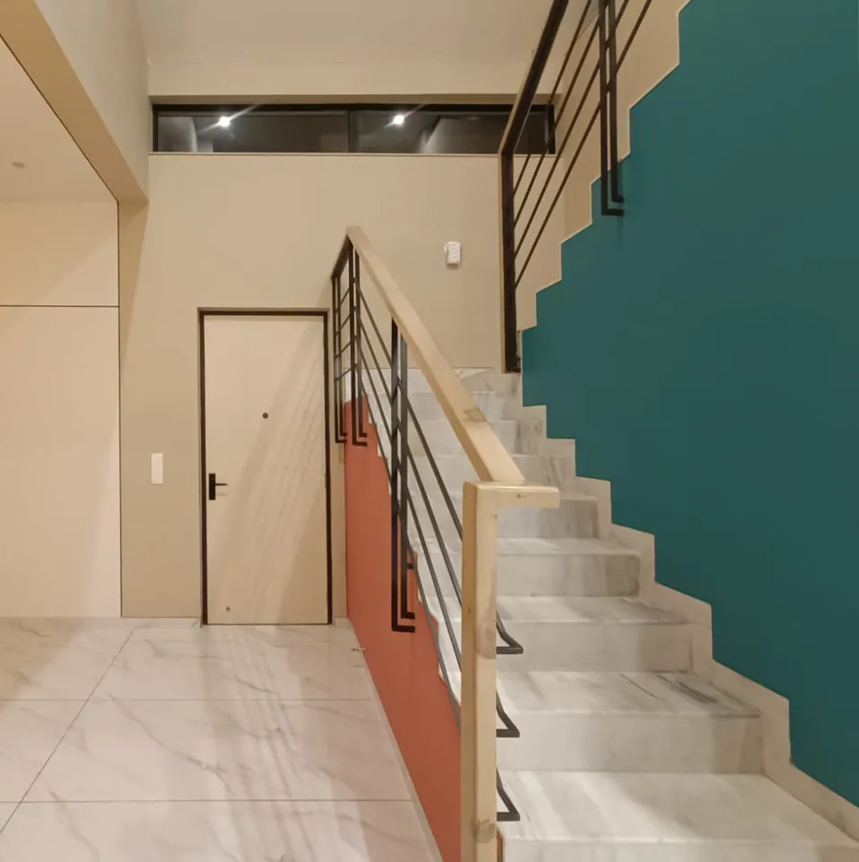 Marble stair rising along a teal wall with a coral strip, timber handrail and black balusters, a white door beside it