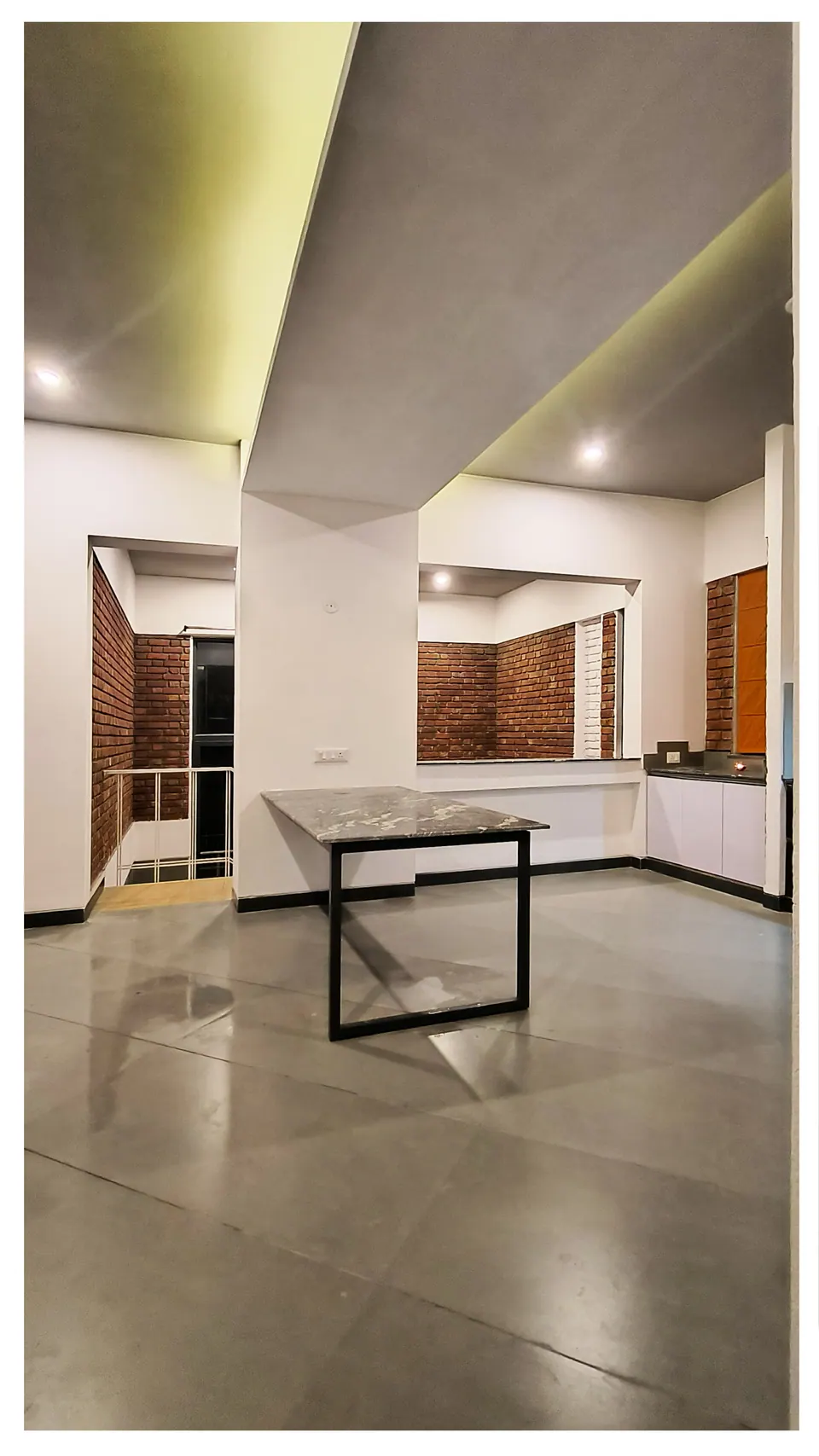 Dining table with a dark stone top beneath a beam, the kitchen and brick-framed openings beyond