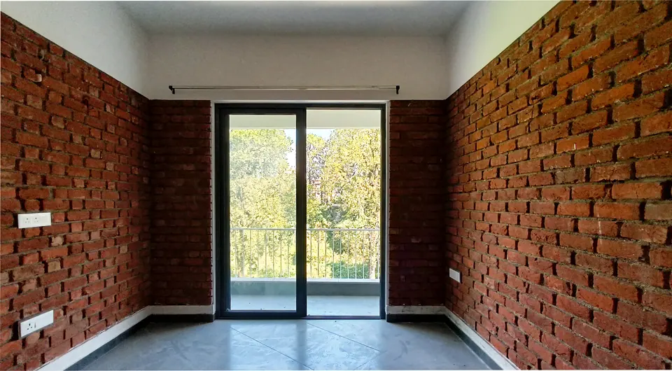Room with exposed brick walls and a glazed door opening onto a balcony and trees